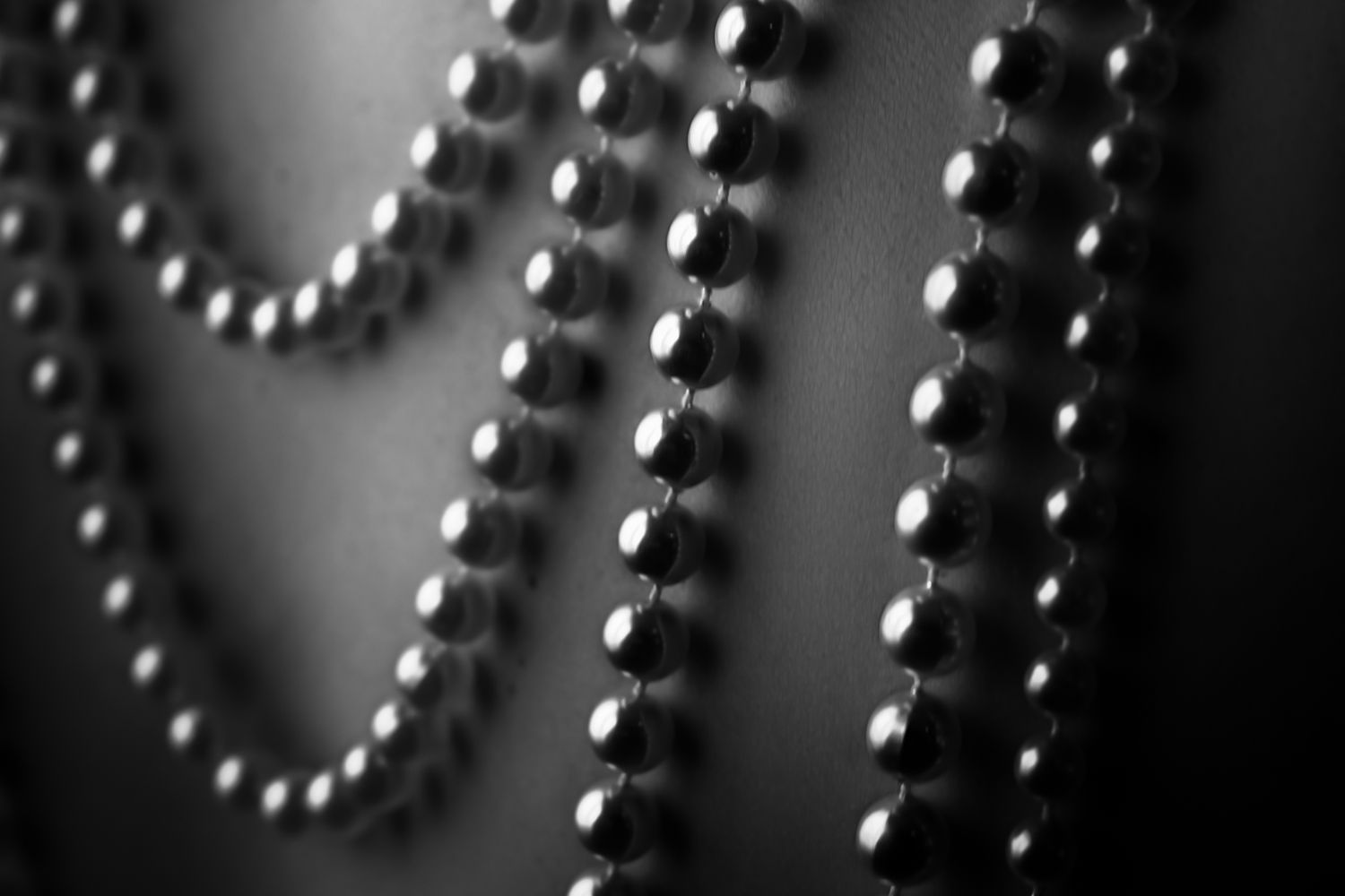 Close-up black and white photo of elegant pearl bead strands draped gracefully against a dark background.