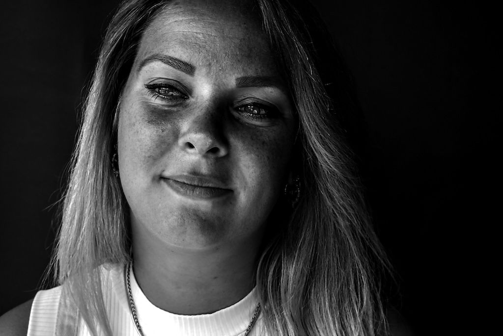 Zwart-witportret van een jonge vrouw met lang haar, die zachtjes glimlacht tegen een donkere achtergrond.
