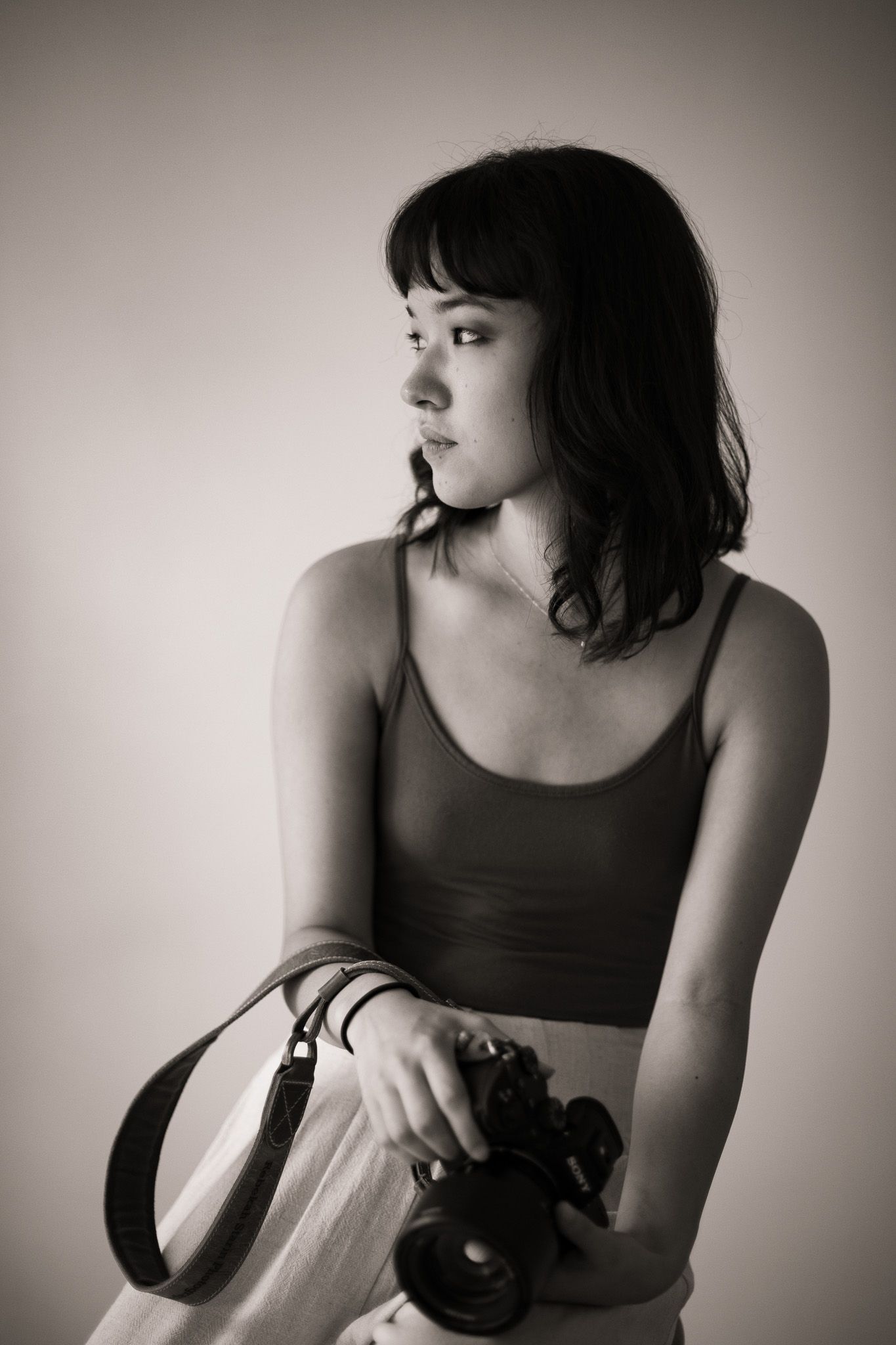Picture of Rebekah Starin Photography. Rebekah sitting on a chair holding her camera and looking over her shoulder.Black