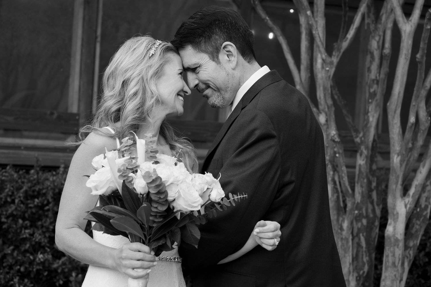 Bride and groom have their for-heads together and are smiling at each other. Bride is holding her white rose bouquet. Ph