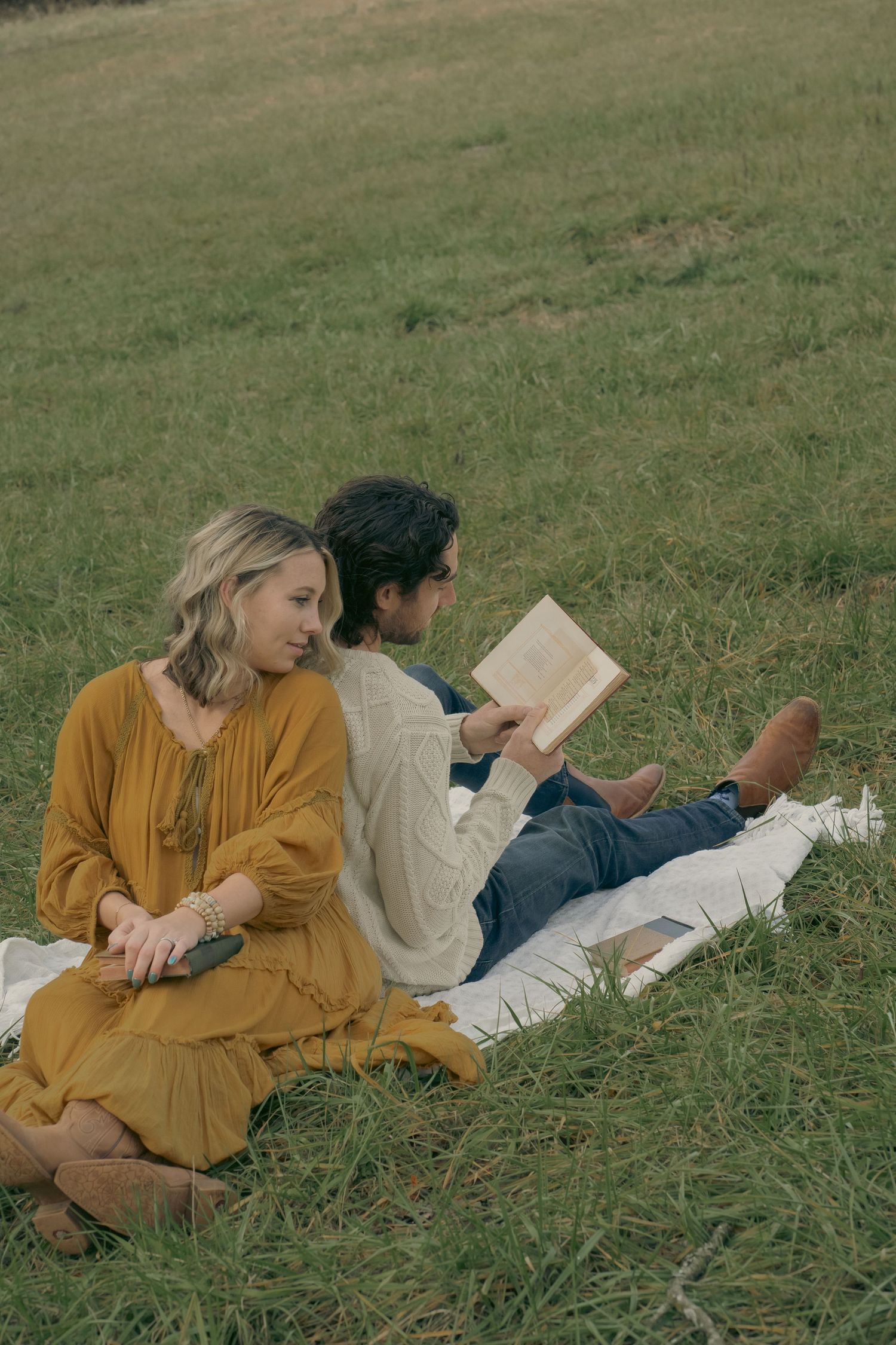 Woman in yellow dress holding a book in her lap while she is back to back with her husband who has a white sweater on an
