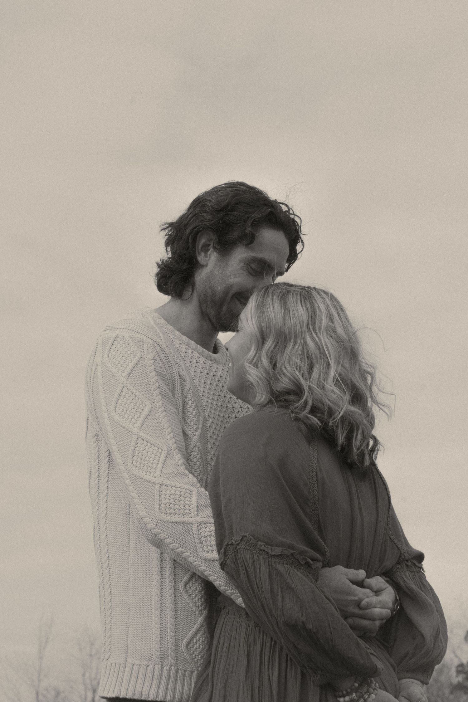 Couple snuggling up to each other for cute for-head kisses. Black and white photo.