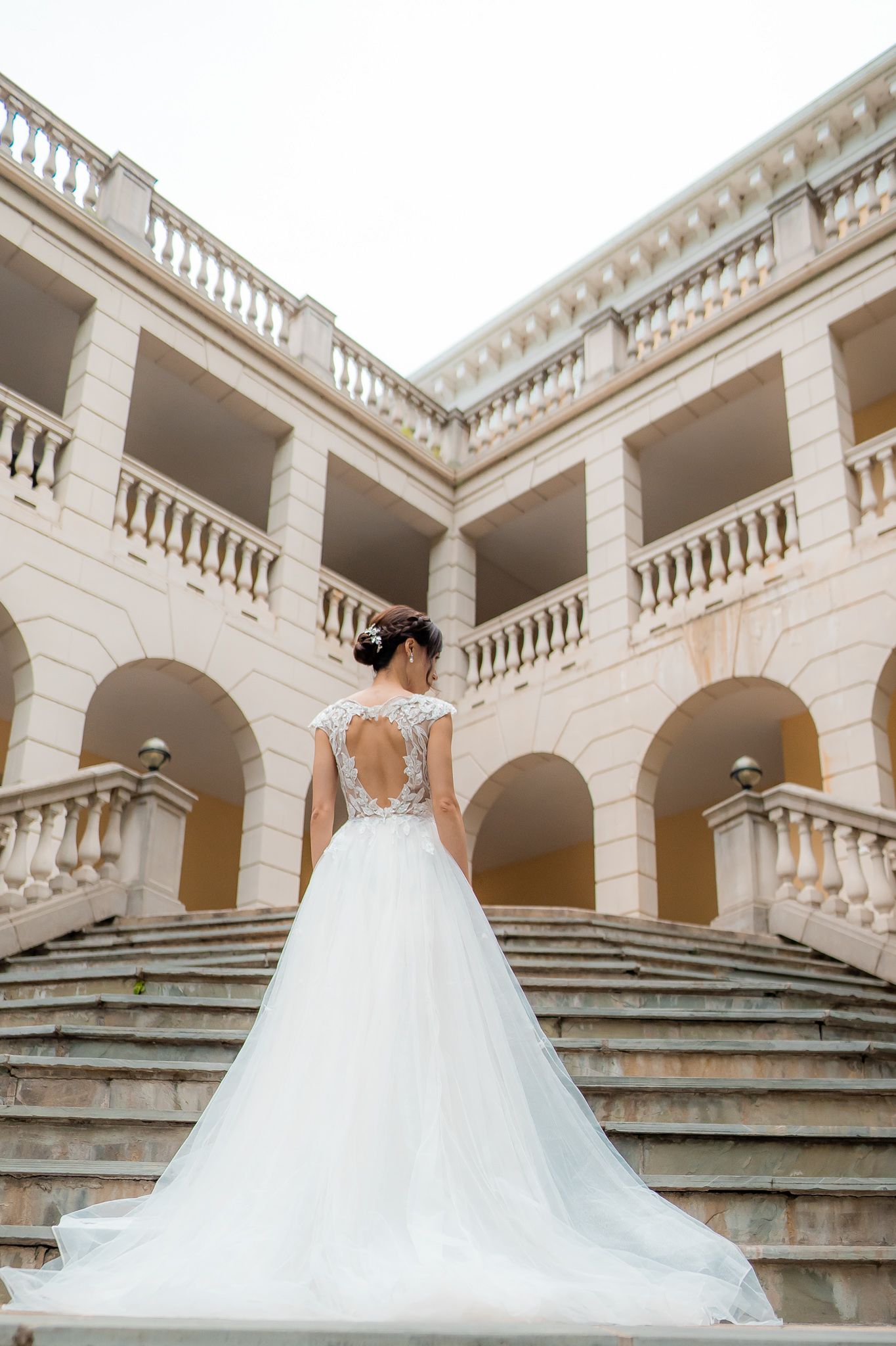 Bride in elegant white dress standing on a stairwell leading up to a grand building. Venue was Airlie in Warrenton, Virg