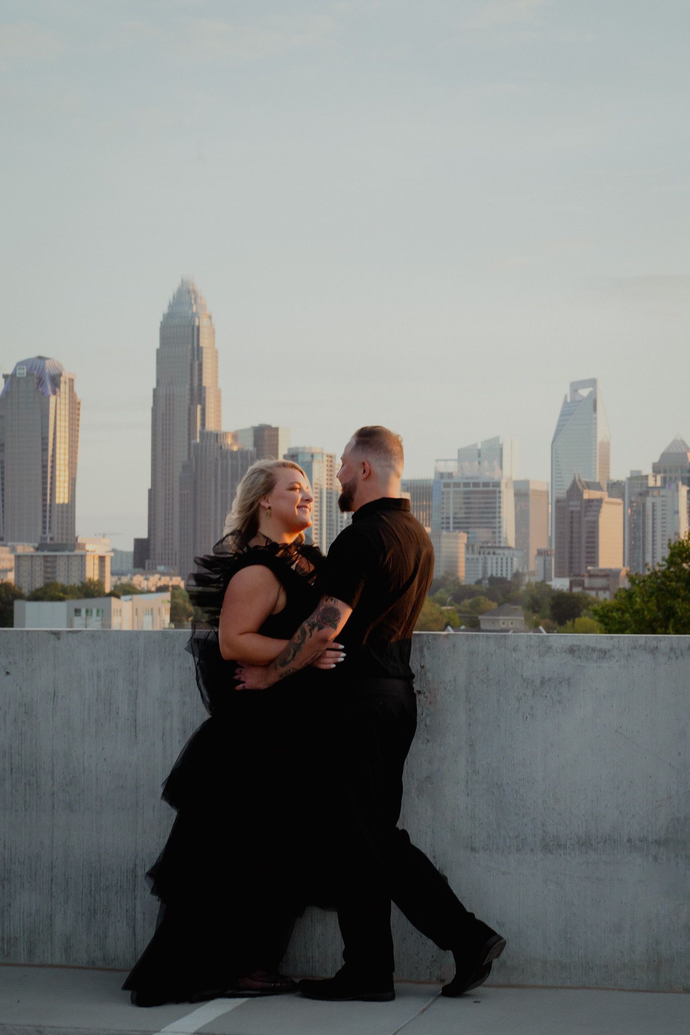 Couple wearing black embracing with the background being the skyline of Charlotte, North Carolina