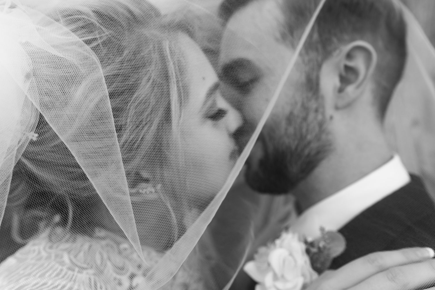 Bride anf groom underneath her veil having a cute kiss. Photo is in black and white.