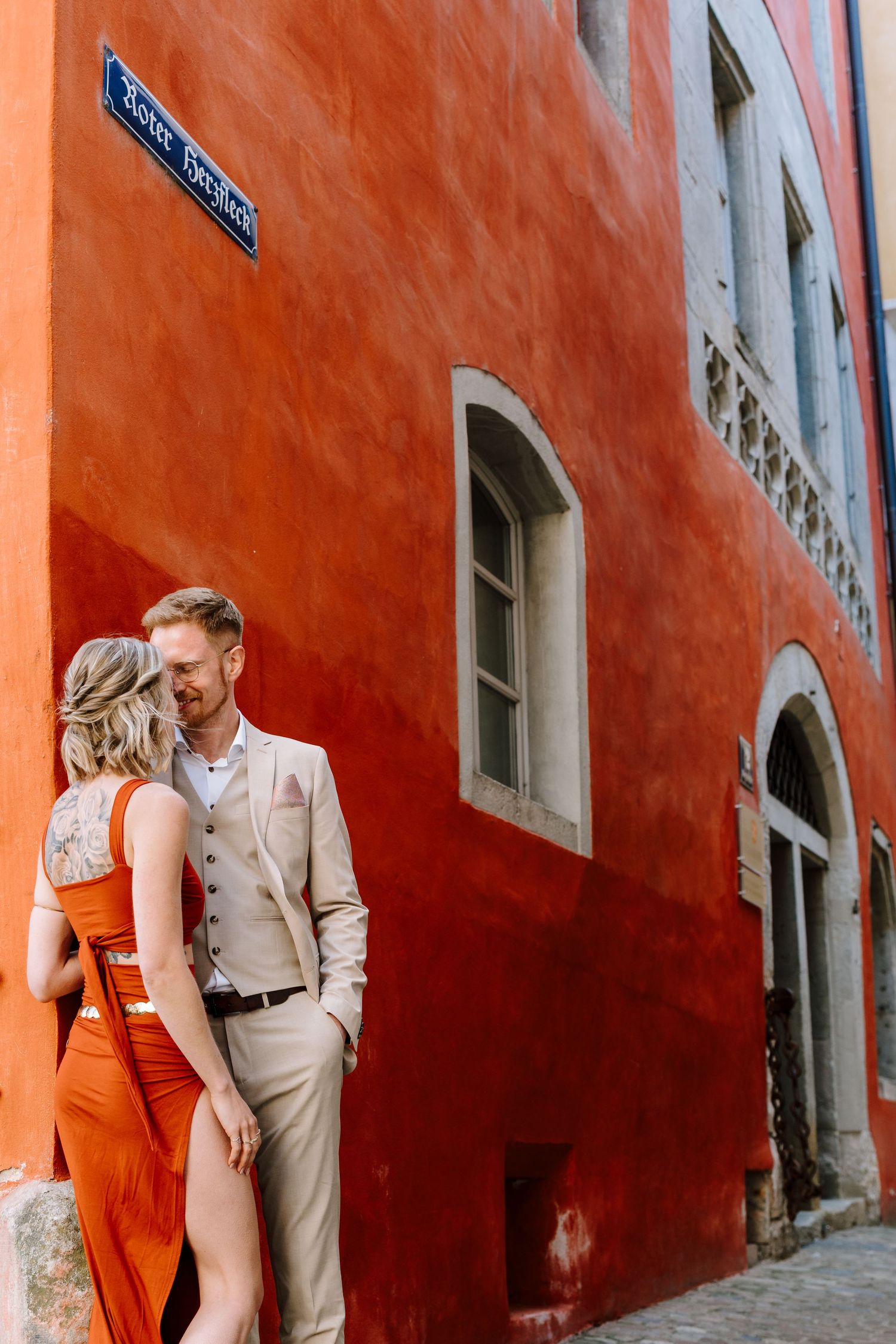 Brautpaar vor einer roten Hausfassade in der Altstadt von Regensburg – natürliches Paarshooting am Hochzeitstag.