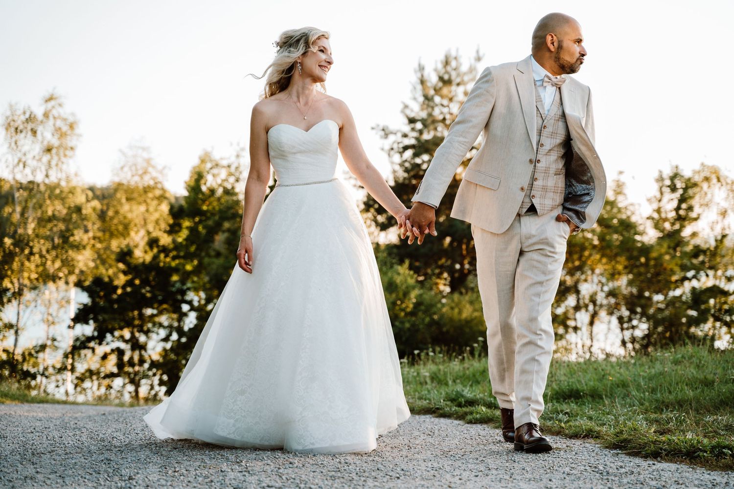A couple in wedding attire walks together during golden hour in a scenic outdoor setting.