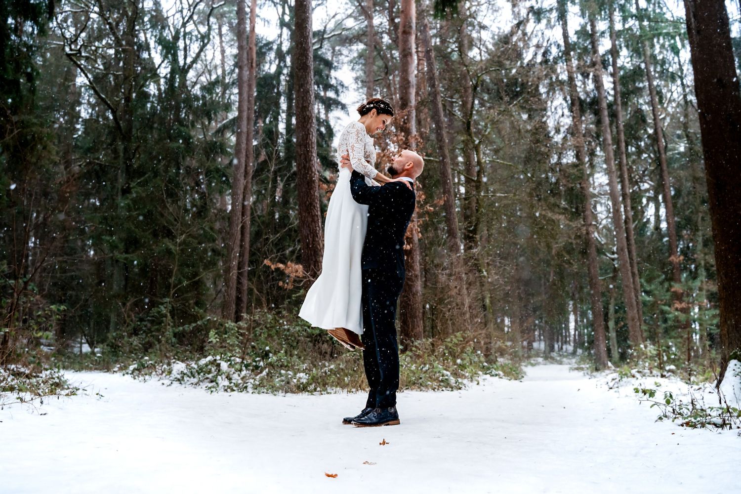 After-Wedding-Shooting im Winterwald im Landkreis Regensburg. Bräutigam hebt die Braut im Schnee.