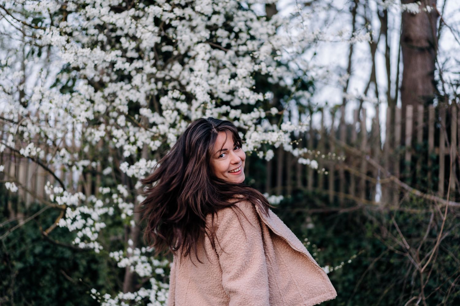 Hochzeitsfotografin Georgina aus Regensburg steht lachend vor blühenden Kirschbäumen im Frühling – natürliches Portrait in der Natur