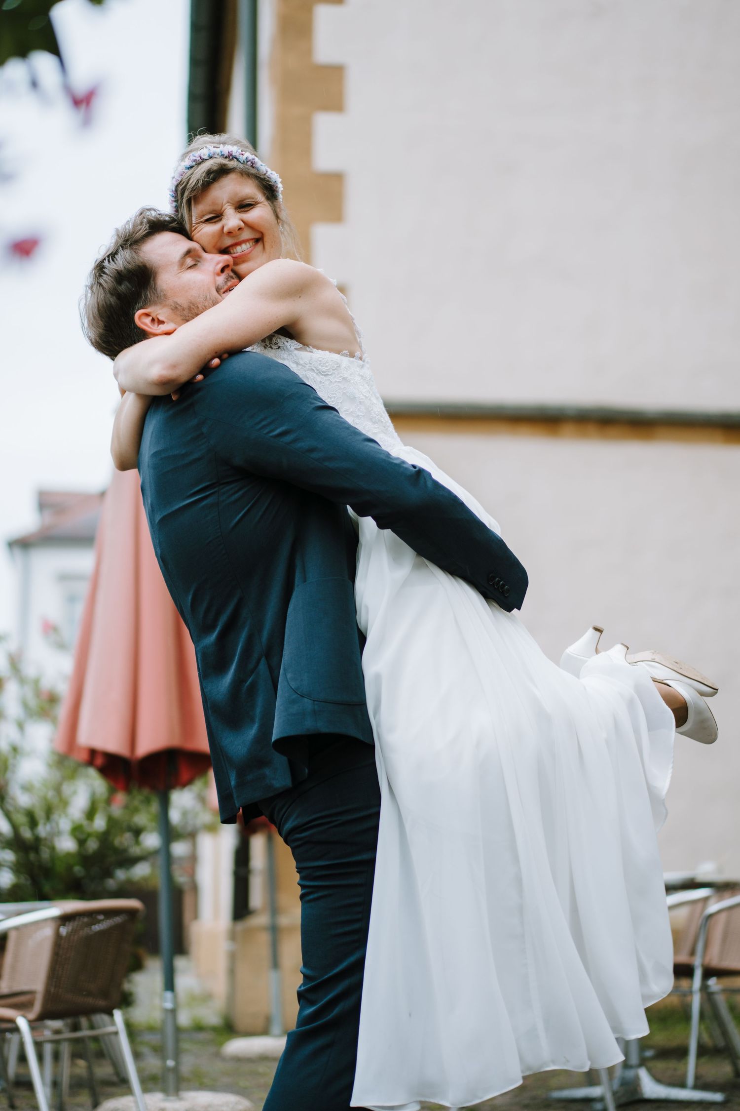 Bräutigam hebt lachende Braut hoch – lebendige Hochzeitsmomente im Freien.