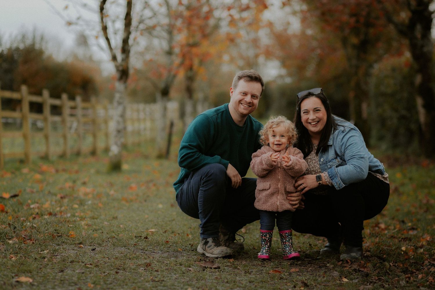 Family crouching together on autumn path surrounded by fallen leaves.