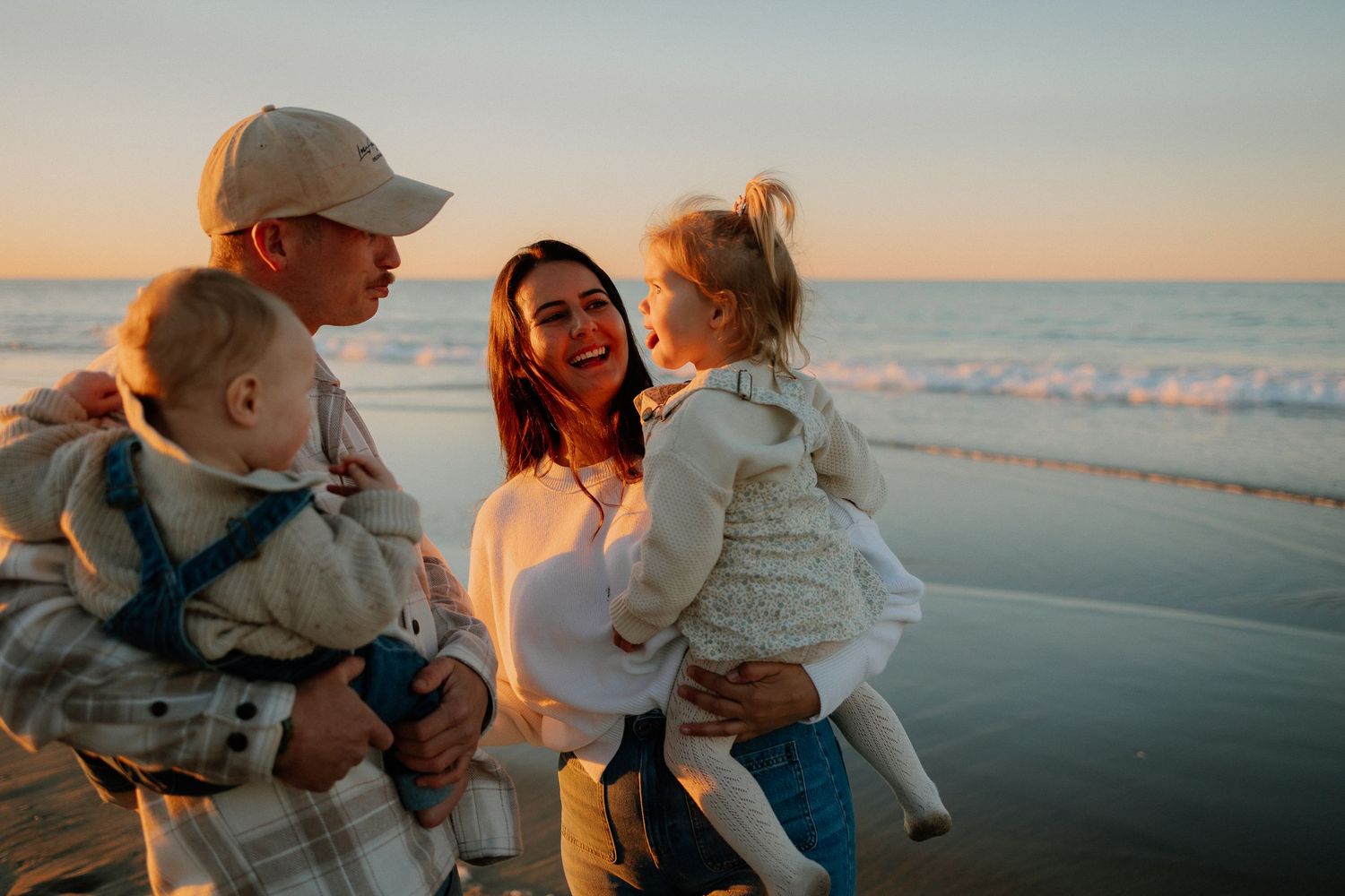 A family embraces on a beach at sunset while waves gently roll onto the shore in the golden light.