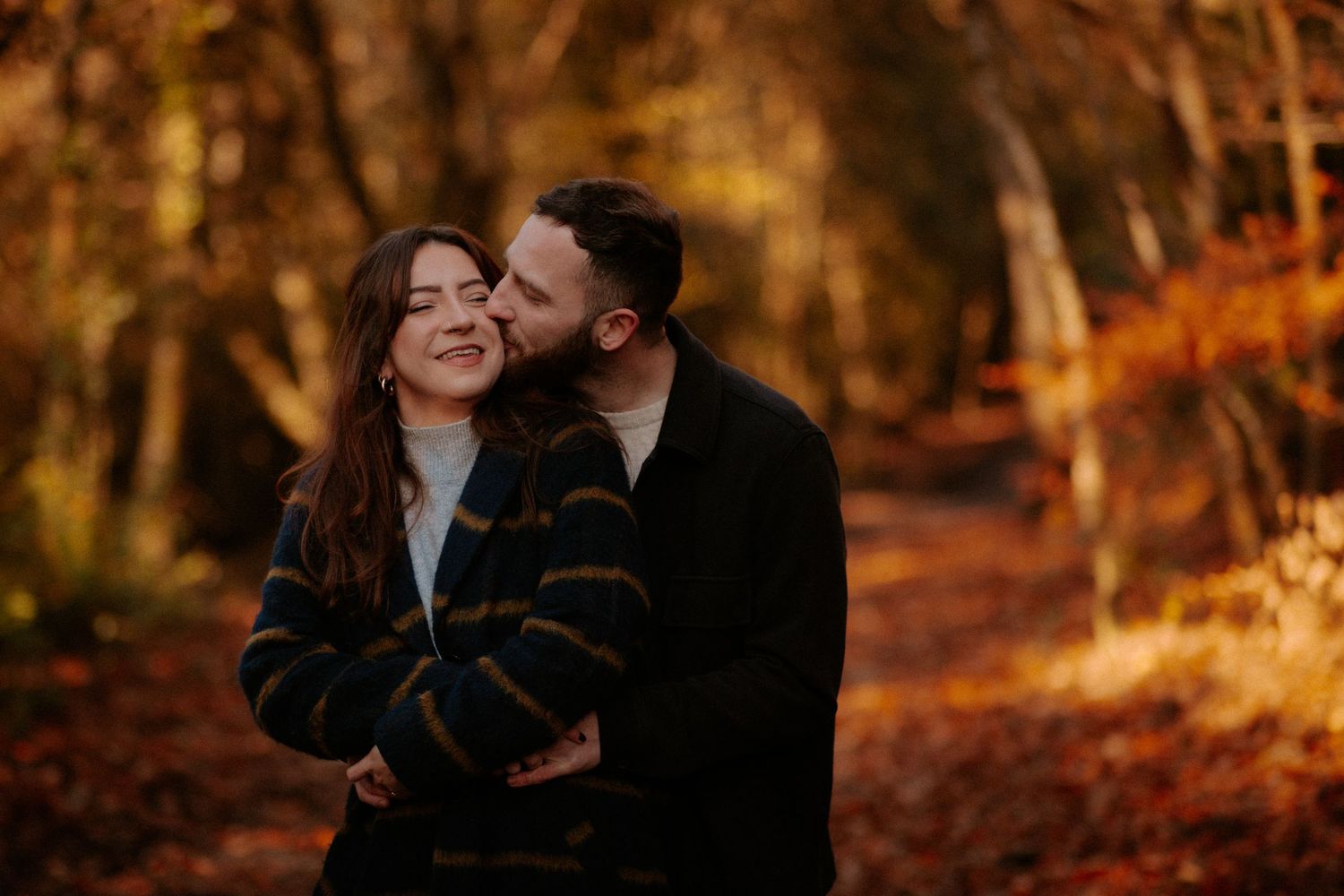 Couple sharing intimate moment on path surrounded by golden autumn foliage.