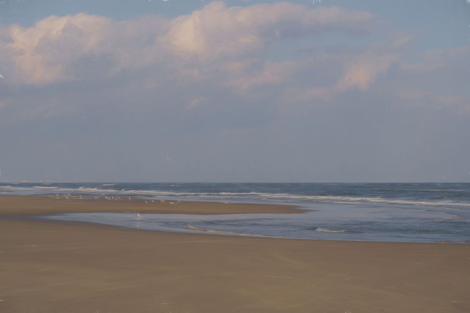 Panoramic view of a sandy beach coastline with rolling waves and cloudy sky stretching to the horizon.