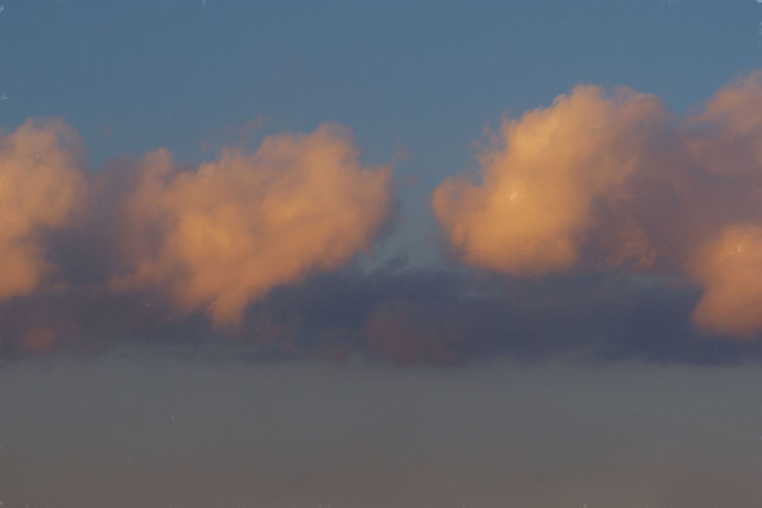 Fluffy pink and orange clouds float against a dusky blue sky during sunset.