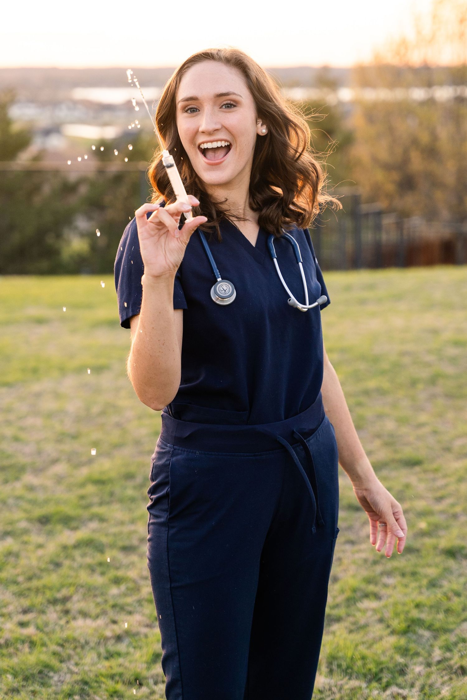 Grad Session  for a nurse in DFW, Texas. Girl smiles and shoots water out of a syringe while wearing scrubs.