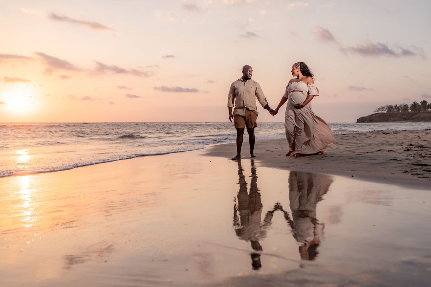 Expectant couple strolling hand in hand along sunset beach, golden reflections on wet sand below. Guanacaste, Costa Rica