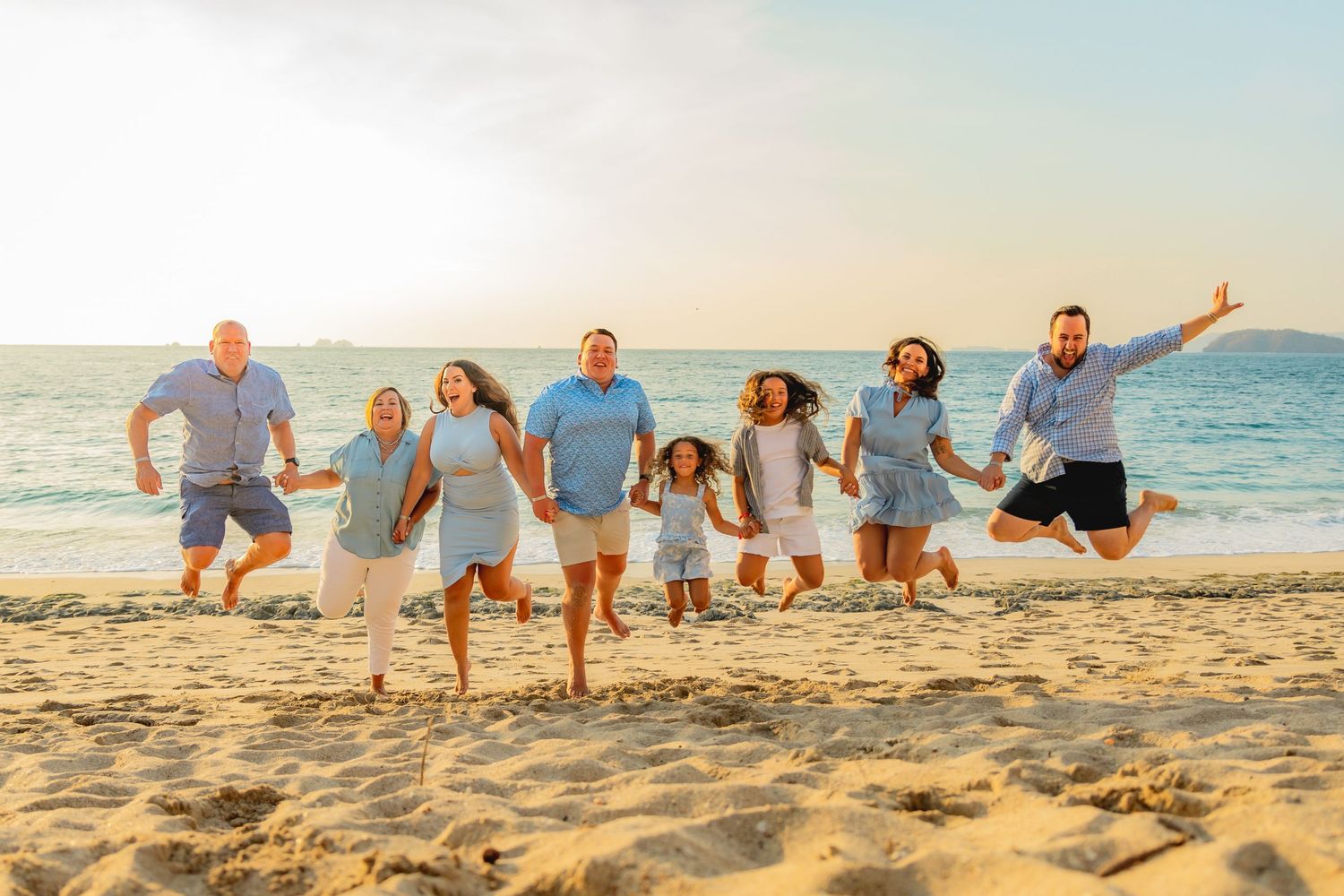 Large extended family in matching blue outfits jumping joyfully together on sunny beach at sunset. Guanacaste, Costa Rica