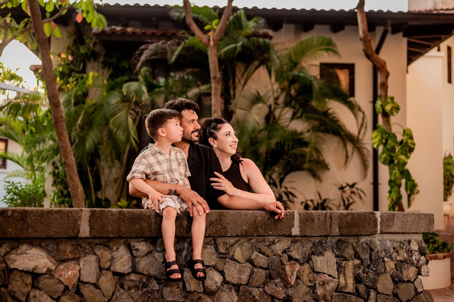 Young family sitting together on stone wall surrounded by tropical resort architecture at dusk. Guanacaste, Costa Rica