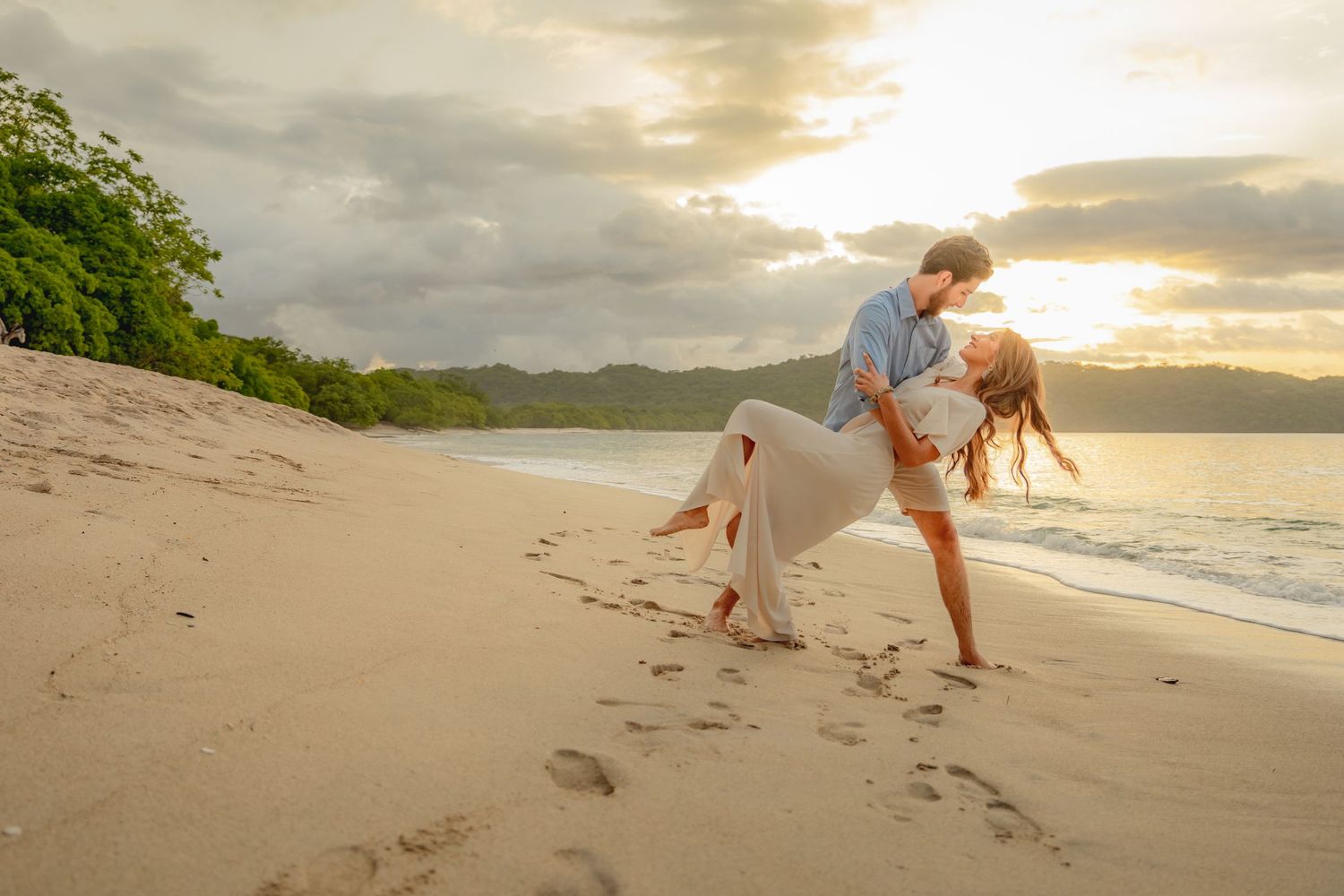 Romantic couple dancing on sandy beach at dramatic golden sunset with ocean waves nearby. Guanacaste, Costa Rica