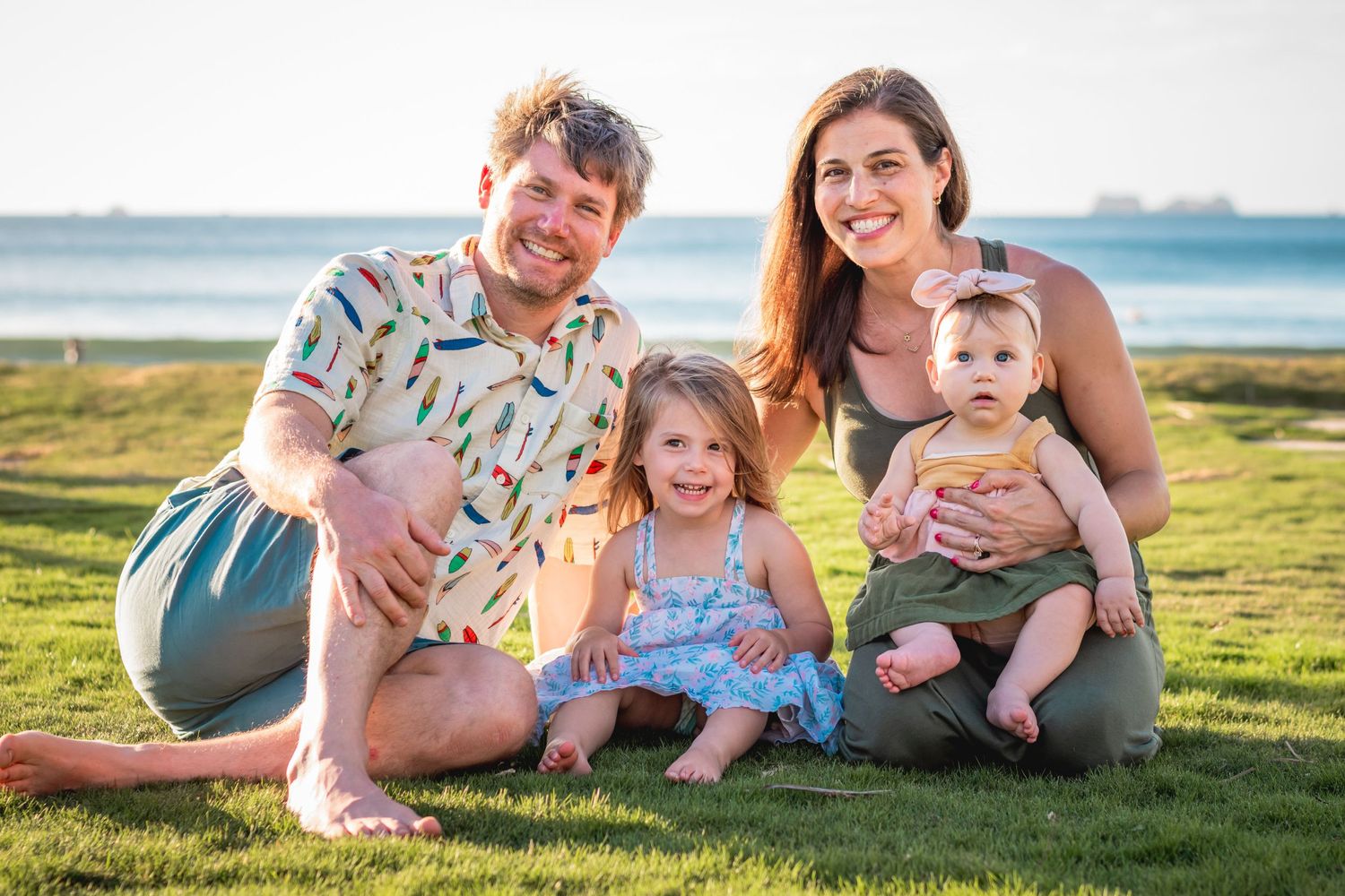 Young family with two small children smiling together on green grass near ocean at sunset. Guanacaste, Costa Rica