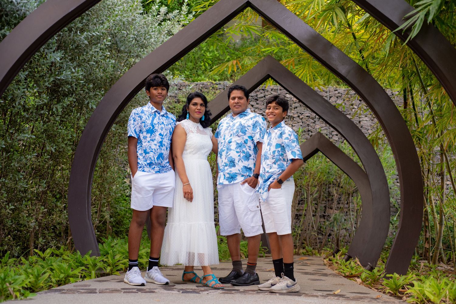 Family of four poses under decorative arch in lush garden, wearing coordinated blue floral and white outfits. Guanacaste, Costa Rica