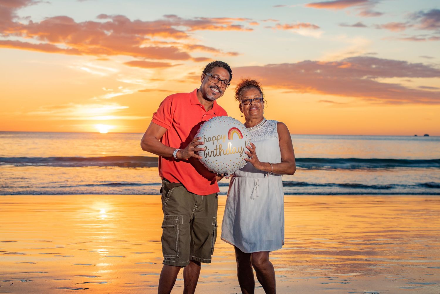 Couple holds Happy Birthday balloon on beach at golden sunset. Guanacaste, Costa Rica