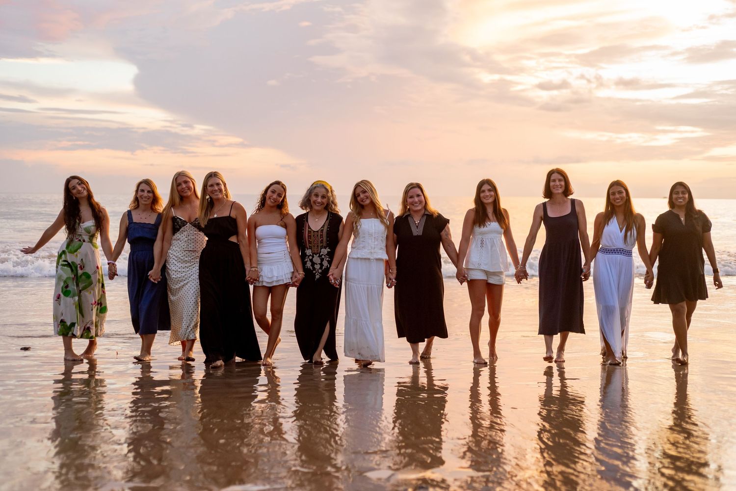 A row of elegantly dressed women holding hands and walking along a beach at sunset. Guanacaste, Costa Rica