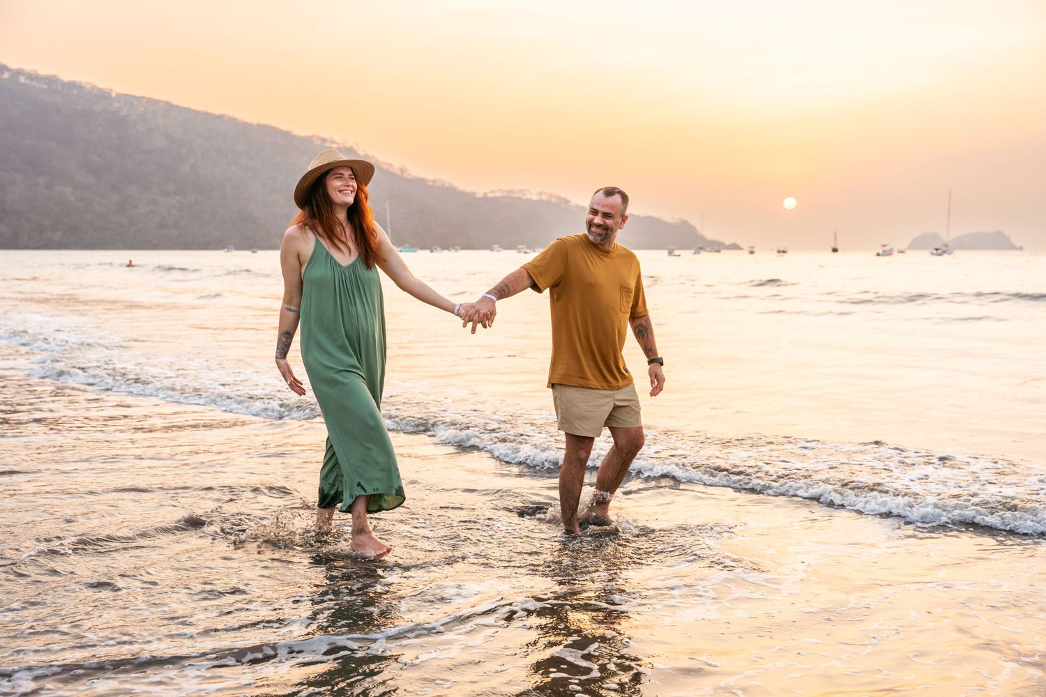 Couple holding hands walking in ocean waves at sunset on beach. Guanacaste, Costa Rica