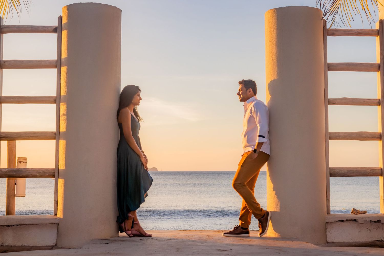 Couple facing each other between pillars with ocean sunset backdrop. Guanacaste, Costa Rica