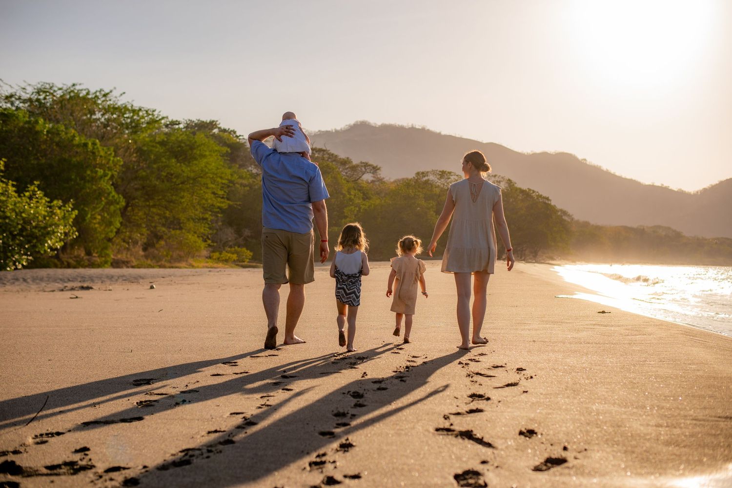 Family walking along sandy beach at golden sunset leaving footprints. Guanacaste, Costa Rica