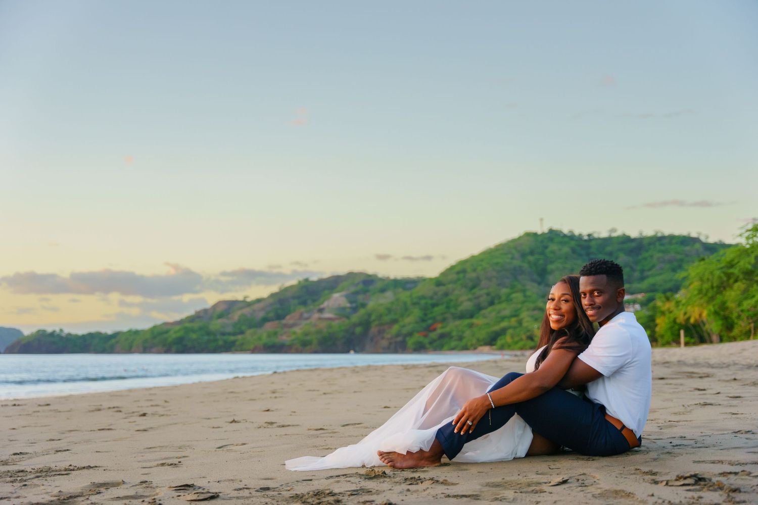 Couple sitting back-to-back on sandy beach at sunset. Guanacaste, Costa Rica