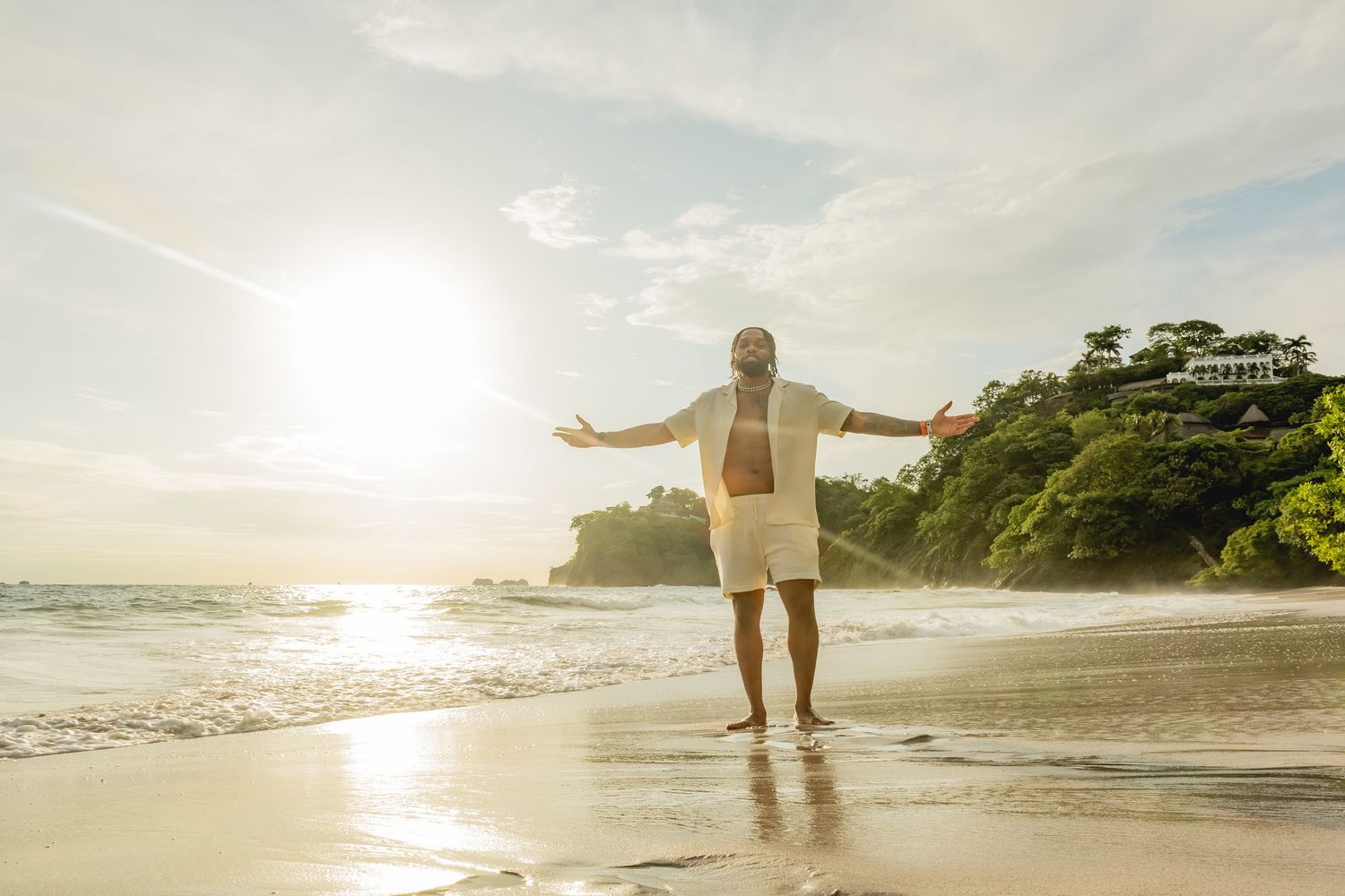Man standing on a sunny beach with arms outstretched at golden sunset with lush green hills. Guanacaste, Costa Rica
