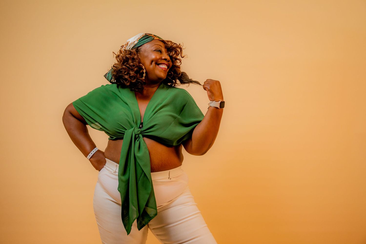 Confident woman in green tied crop top and white pants posing on orange background photo studio. Guanacaste, Costa Rica