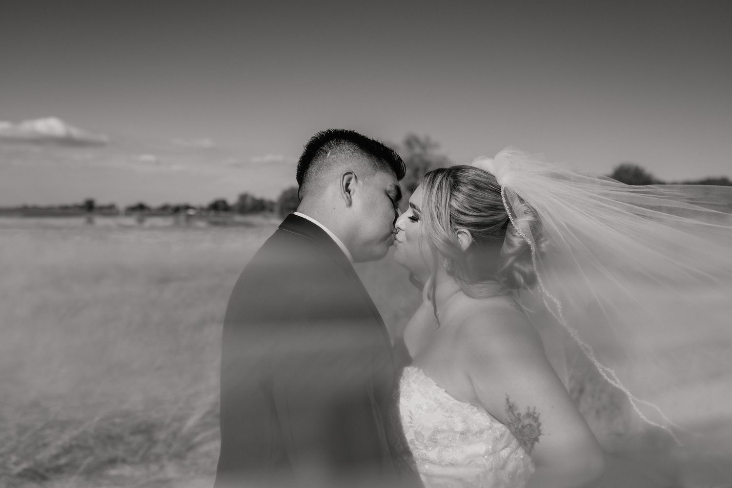 Black and white photo of a romantic wedding couple sharing an intimate moment in a desert landscape.