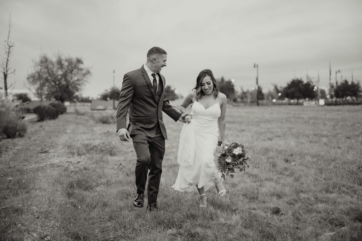 A black and white photo shows a couple running joyfully through a field, with the bride holding a bouquet.