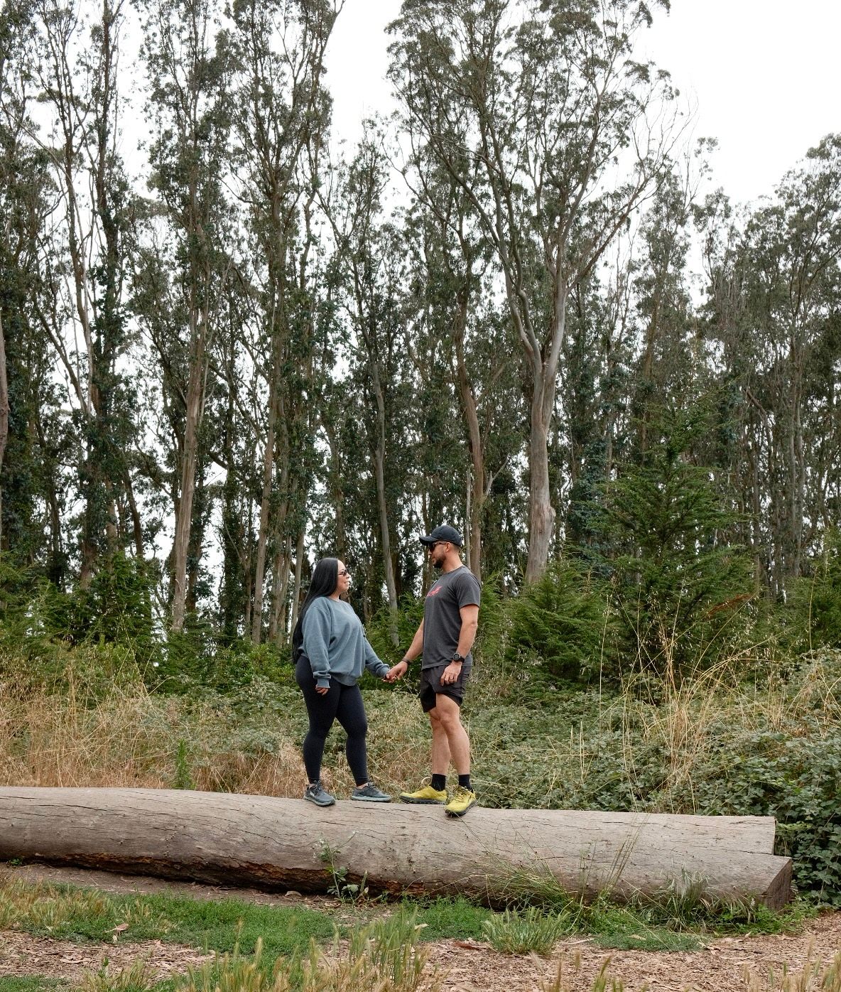 People explore a scenic wooded trail with tall eucalyptus trees and paths leading through a shaded natural area.