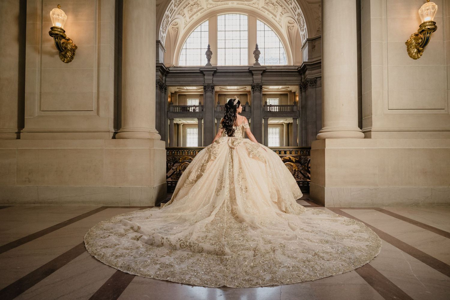 A stunning quince gown with an ornate cathedral-length train photographed in an elegant marble hallway with arched windows.