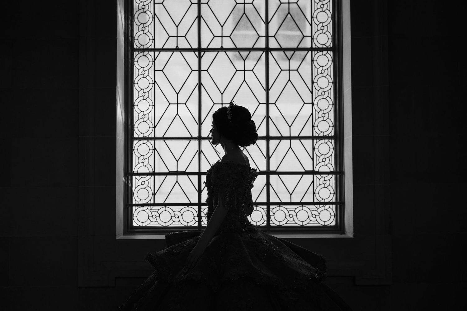 A quinceanera silhouette photograph in front of a geometric patterned window, creating a dramatic black and white contrast effect.