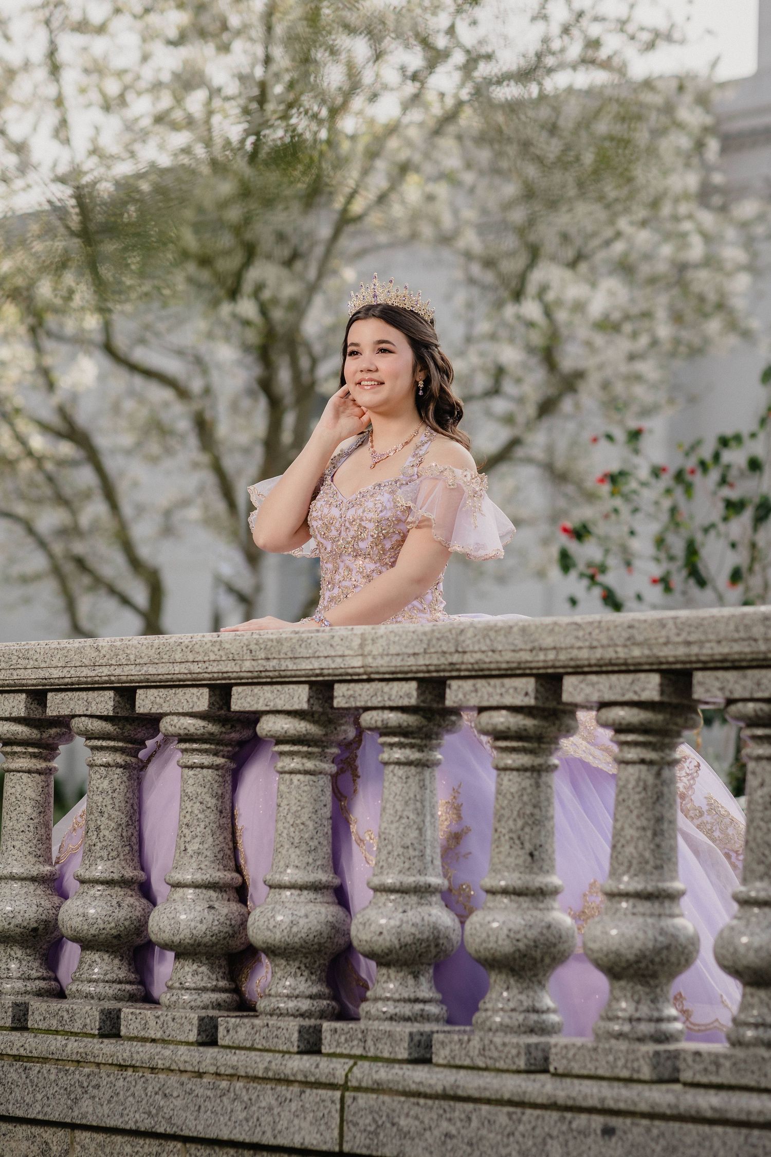 A quinceanera in a delicate purple dress poses elegantly by a stone staircase for pre-event session outdoors