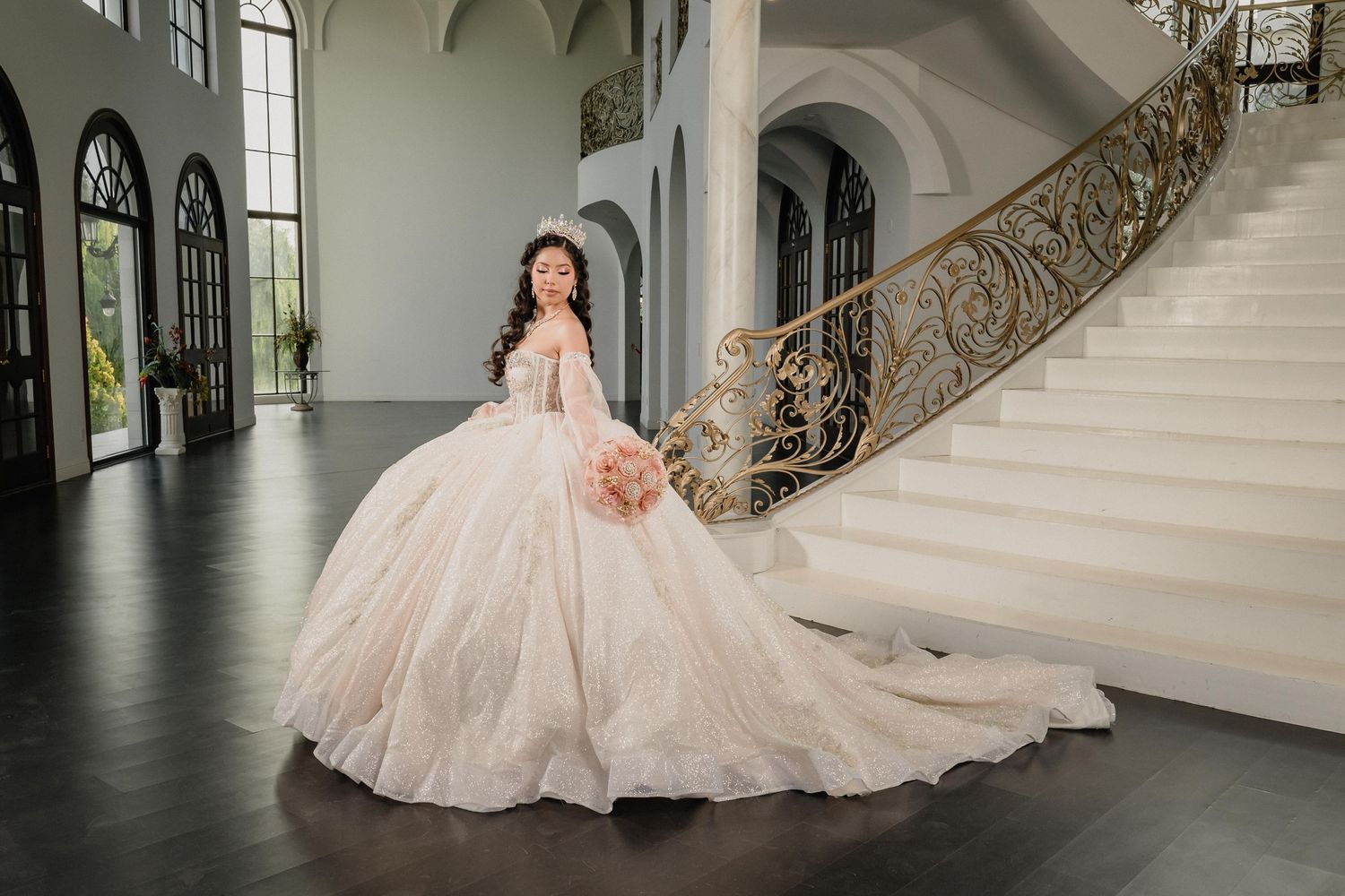A flowing blush pink quince dress with intricate details sits elegantly against a grand staircase in an opulent venue.