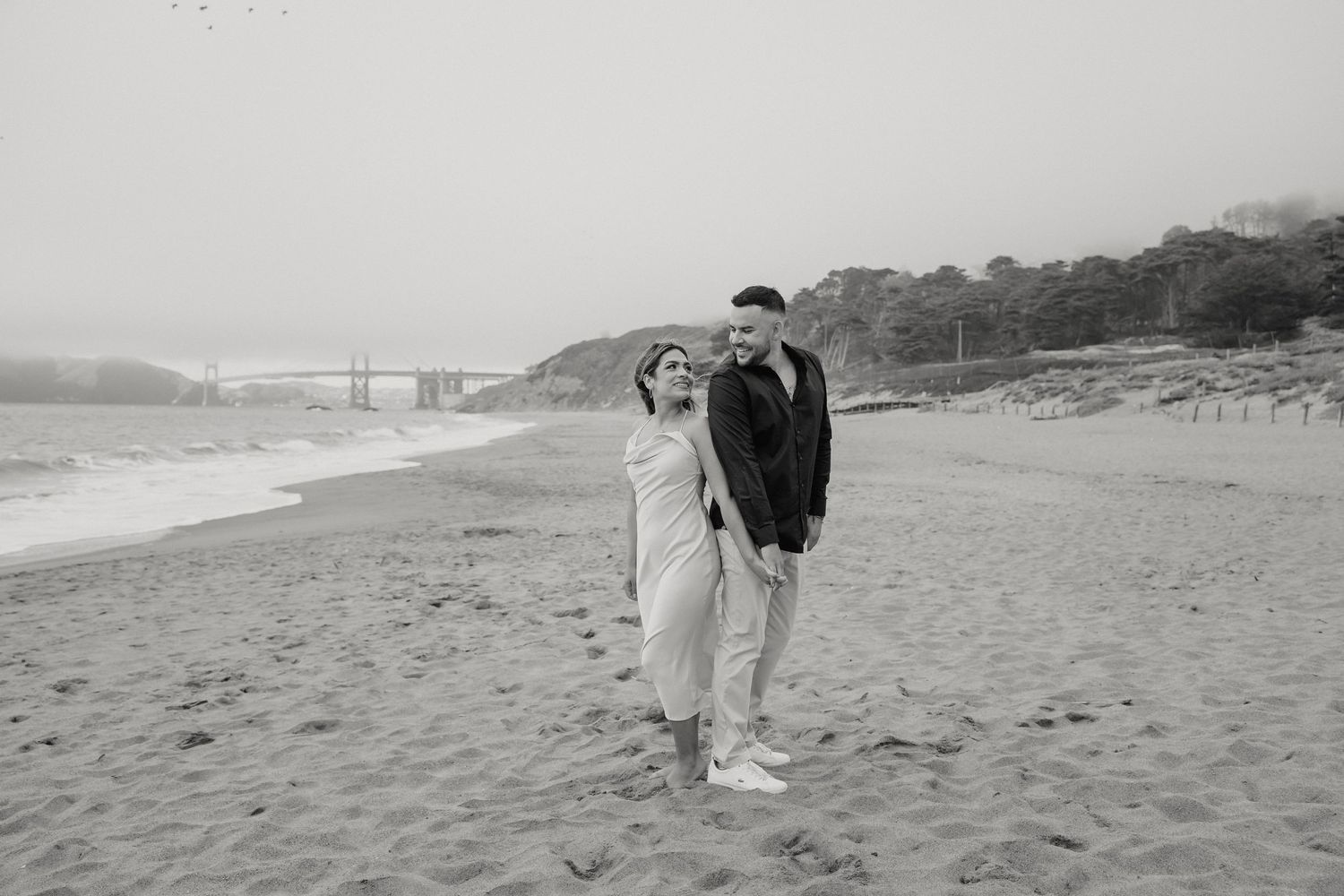 Black and white portrait of a couple walking along a foggy beach.