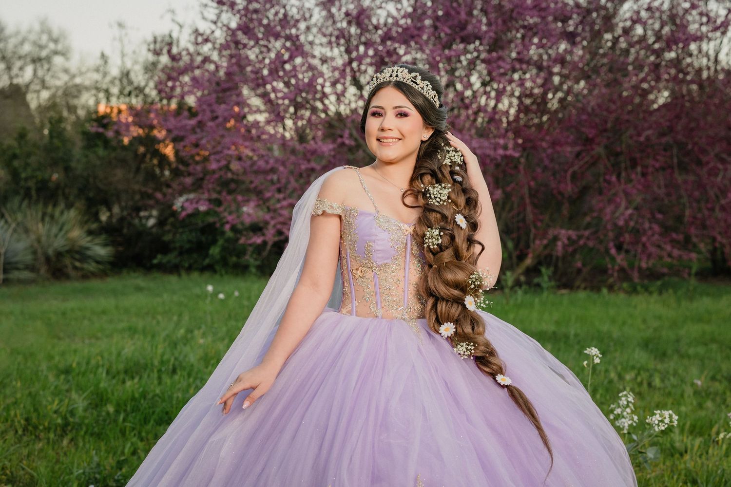 Beautiful lavender quinceanera rapunzel theme and long wavy hair photographed in garden with blooming spring trees.