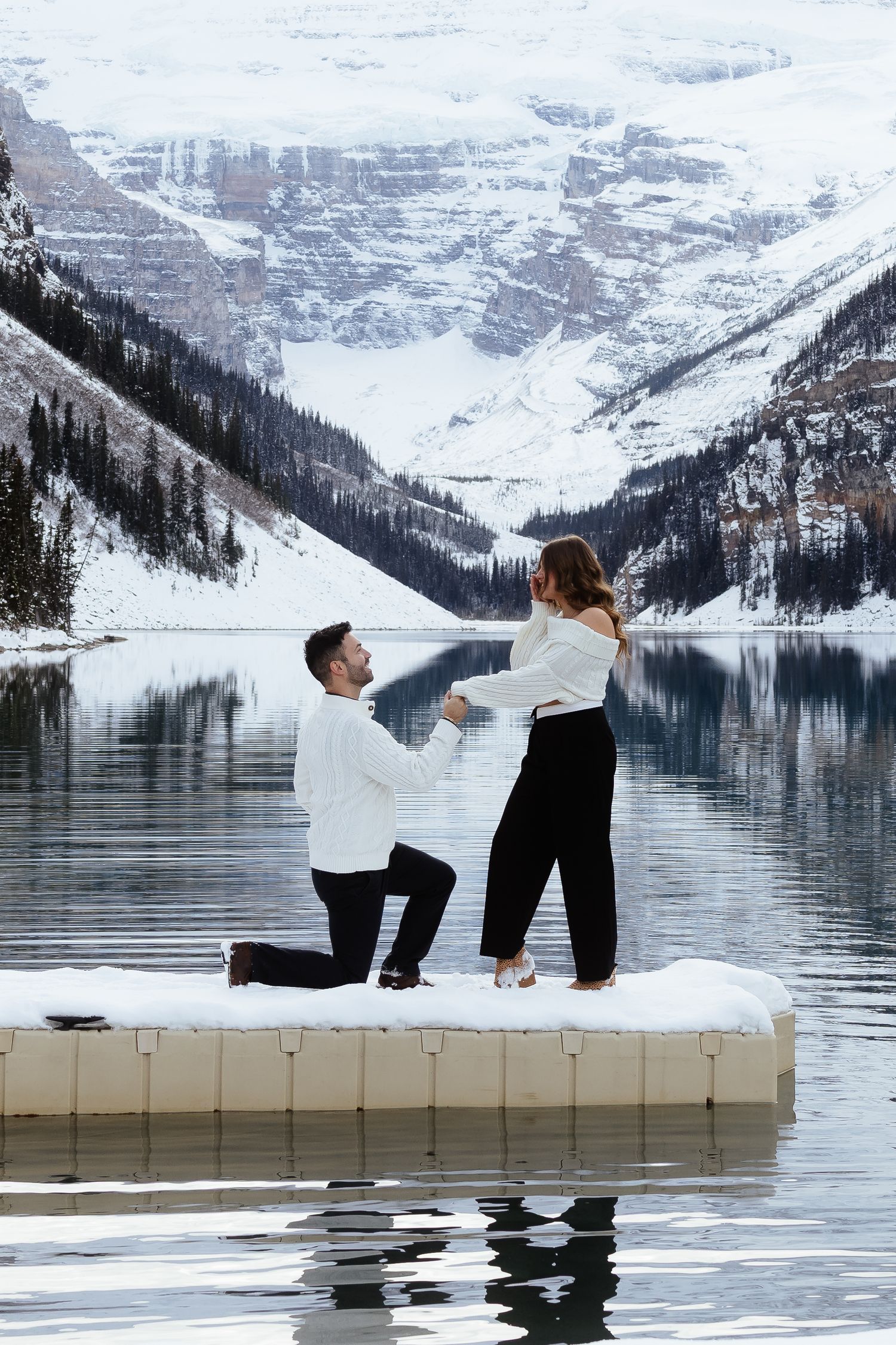 Man proposes on snowy dock at Lake Louise with mountain reflections in winter.