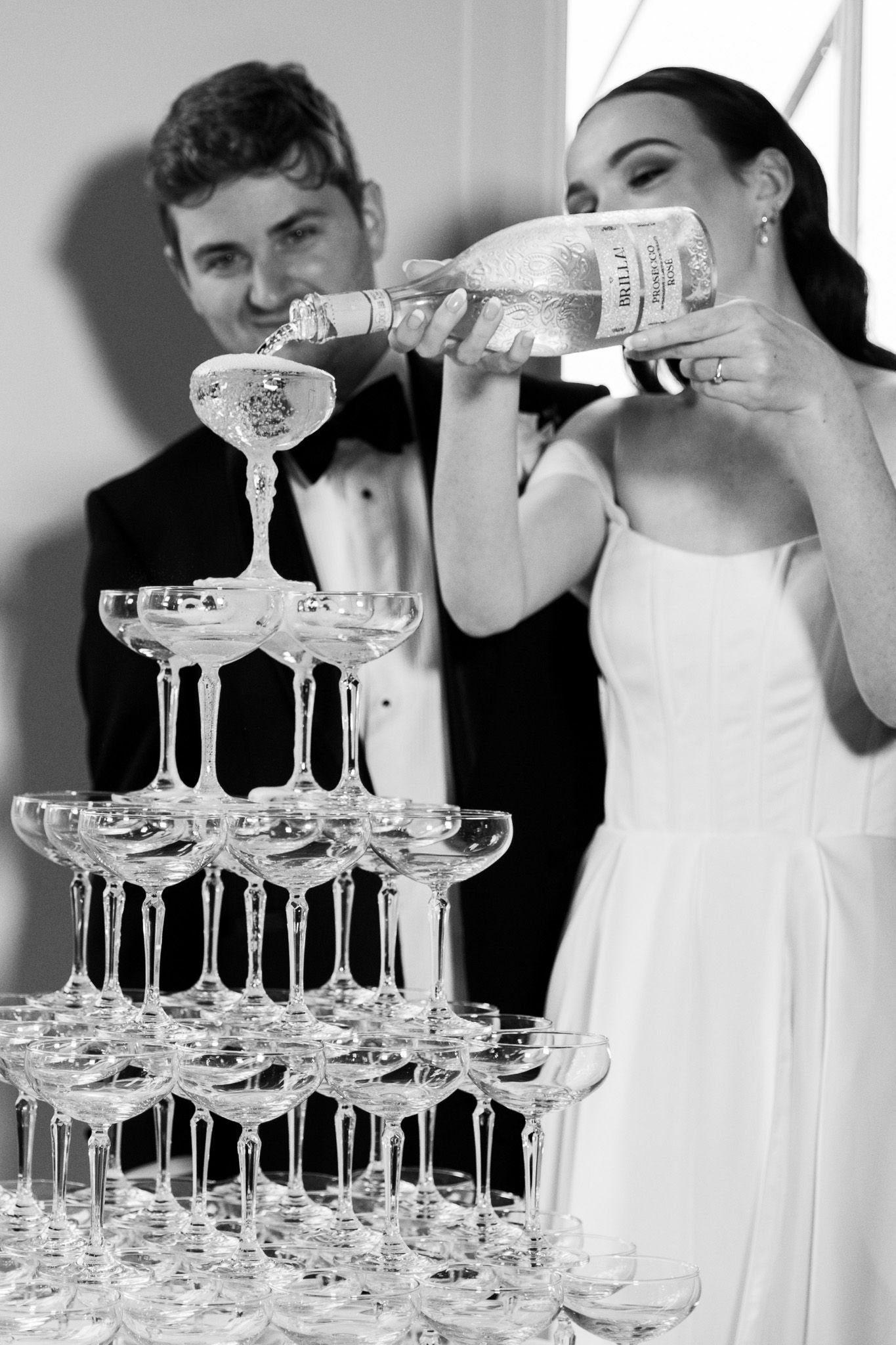 A couple pours champagne into a tower of glasses during their wedding celebration.