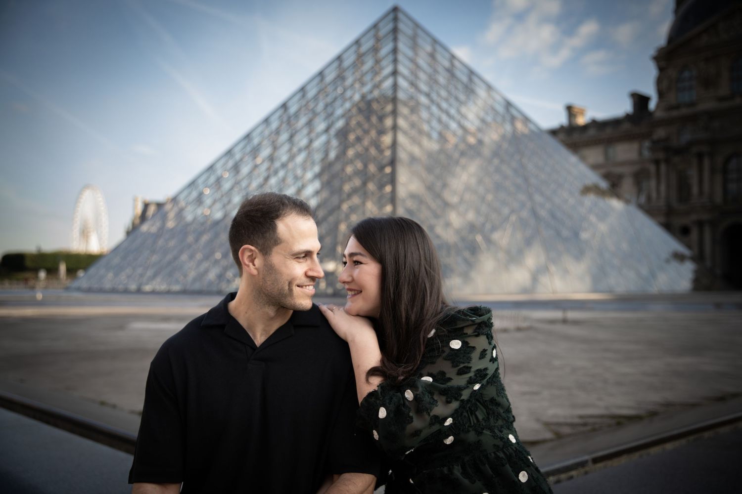 Couple sharing a romantic moment in front of the glass pyramid at the Louvre Museum in Paris.
