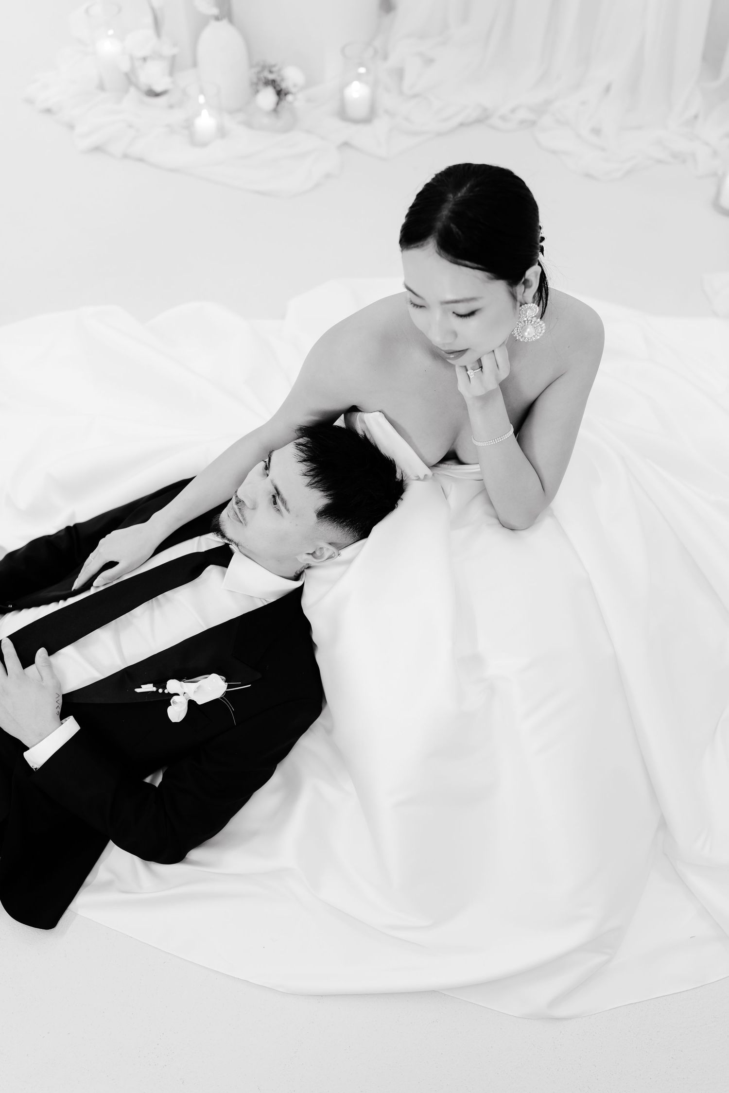 Black and white wedding photo of bride and groom lying on floor, groom resting head on brides lap.