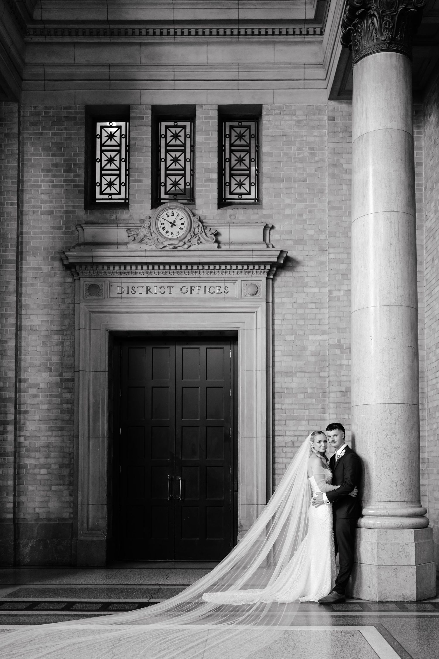 A black and white wedding photo series showing a bride and groom posing dramatically against columns at a district office building.