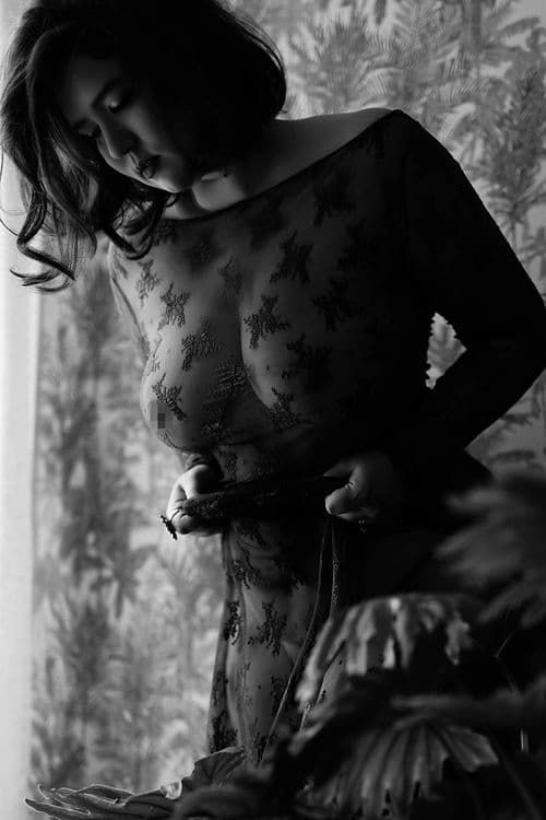 Artistic black and white portrait featuring delicate lace patterns and dramatic shadows against a textured backdrop.