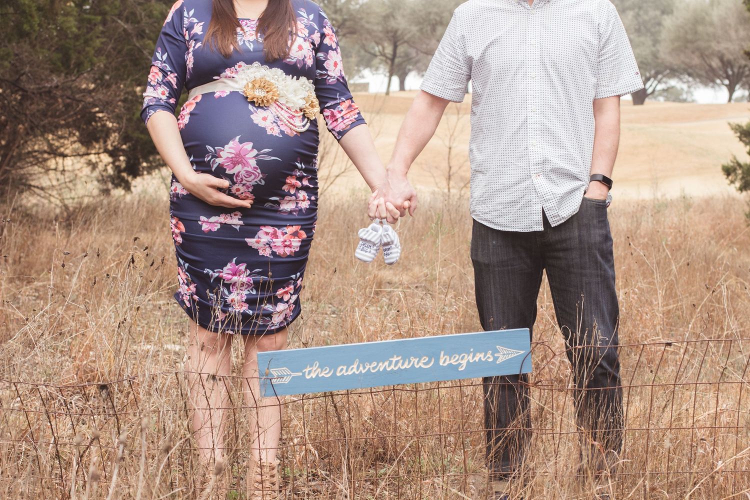 A pregnant couple holding baby shoes and a sign that says 
